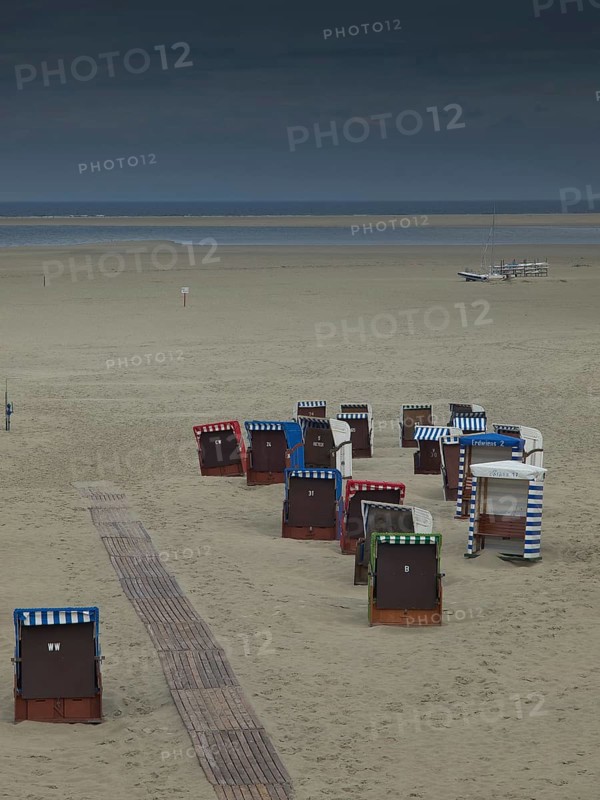 Group of beach chairs on empty, cool beach, cloudy sky and calm atmosphere, beach chairs and beach tents by the sea with cloudy sky, boardwalk in the sand, Borkum, germany