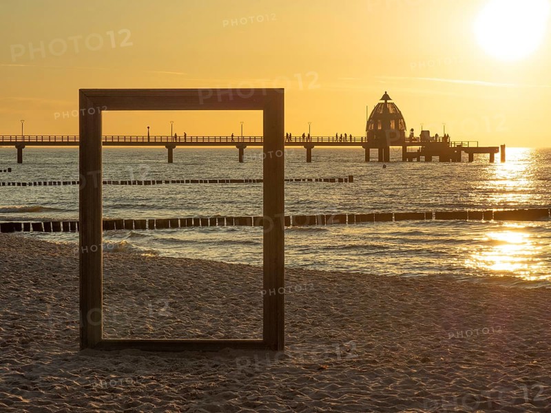 A picture frame on the beach with a view of a pier and the sea at sunset, sunset on a beach with a wooden bridge and beach chairs, Zingst, Germany, Europe