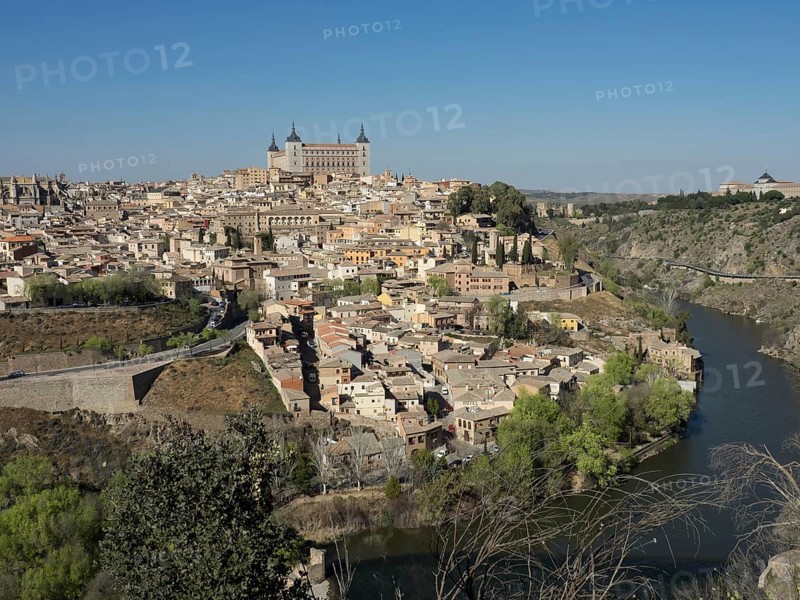 Wide view of a historic city on a river with characteristic church towers and bridges, hills and a clear blue sky, historic city with old houses and big churches on a small river in front of a blue sky, toledo, spain