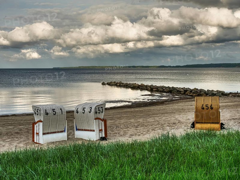 Two white and one yellow beach chair on a sandy beach, rocks in the water and cloudy sky, beach chairs on a quiet sandy beach by the sea, clouds over the sea, Eckernfoerde, germany