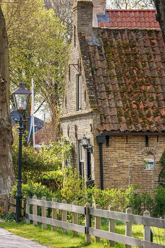 Historic house with tiled roof, fence and street lamp, surrounded by trees in spring, historic houses in a small village with small streets and trees in spring, Nes, Ameland, Netherlands
