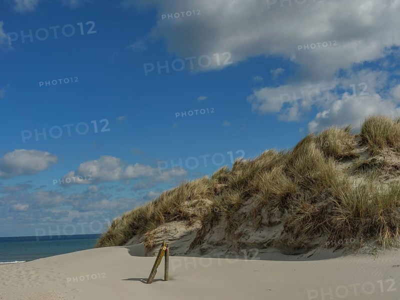 High sand dunes with grass, behind them the sea and a partly cloudy sky, dunes on an island with a blue boat and a bench, clouds and sand by the sea, nees, ameland, the netherlands