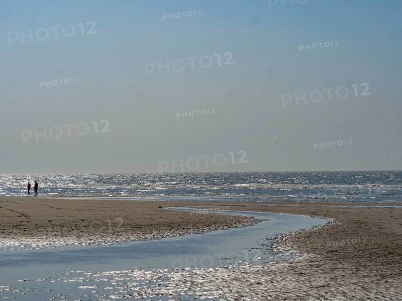 People walking along the beach with a watercourse under a clear blue sky, sparkling sea water at low tide on the beach, de haan, belgium