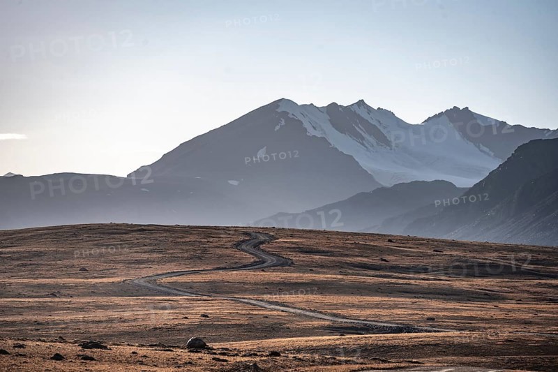 Gravel road through autumnal plateau with brown grass, glaciated and snow-covered peaks, Ak Shyrak Mountains, near the Kumtor Gold Mine, Tian Shan, Kyrgyzstan, Asia