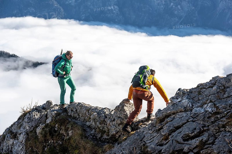 Two hikers at Ettaler Manndl, view over mountain landscape and sea of clouds, high fog in the valley, Ammergau Alps, Bavaria, Germany, Europe