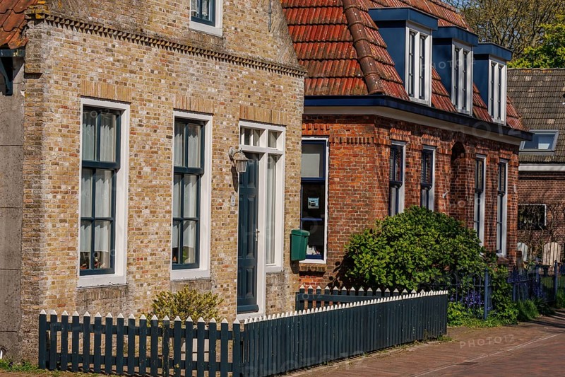 Row of houses with brick facades and white window frames along a quiet street, historic houses and a church with small streets and lanterns, Nes, Ameland, Netherlands