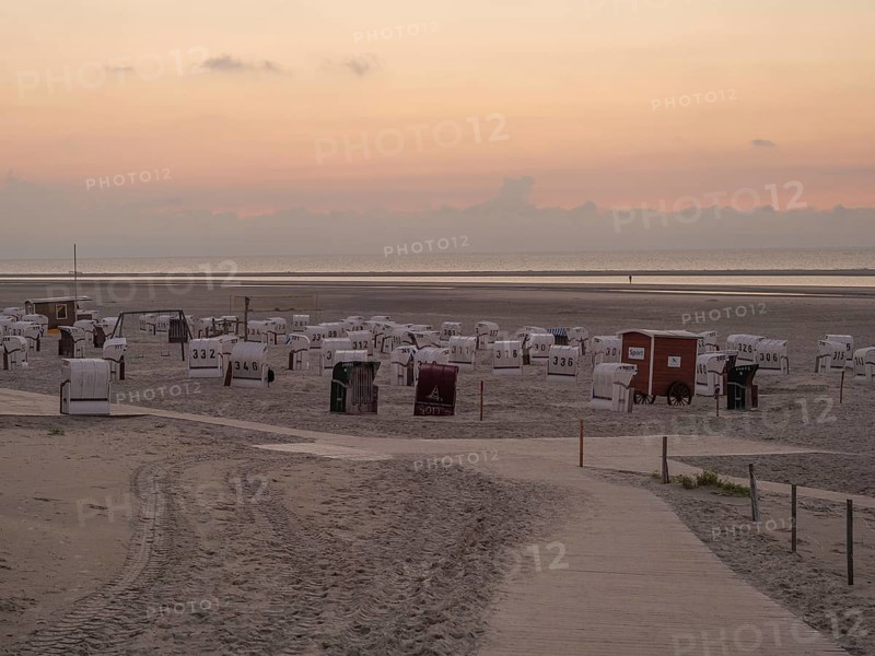 A quiet beach with white beach chairs and a peaceful orange sunset on the horizon, setting sun on a beach with beach chairs and clouds in the sky, spiekeroog, germany