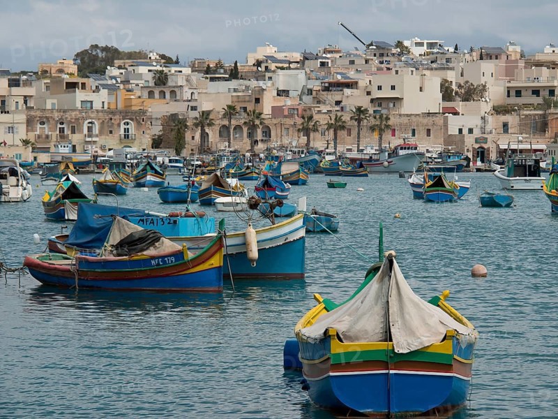 View of a multitude of fishing boats in a busy harbour off the coast of a town, many colourful fishing boats in a harbour in the Mediterranean, Marsaxlokk, malta