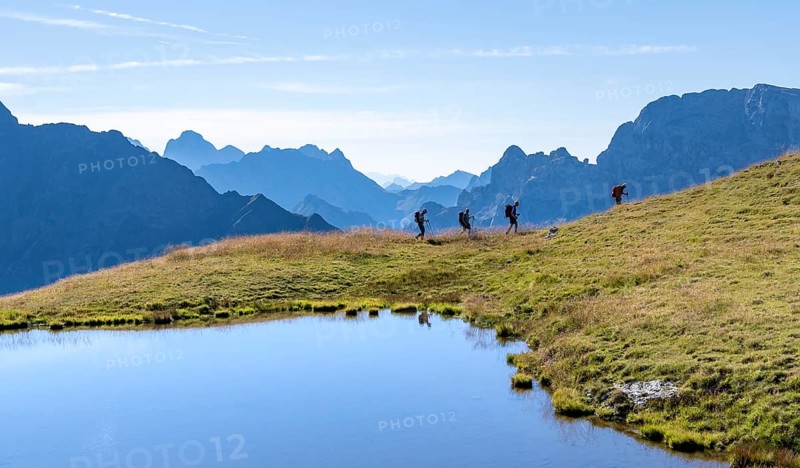 Group of mountaineers in front of mountain landscape, mountain lake and silhouettes of rocky mountain peaks, Luggauer Toerl, Carnic High Trail, Carnic Main Ridge, Carnic Alps, Carinthia, Austria, Europe
