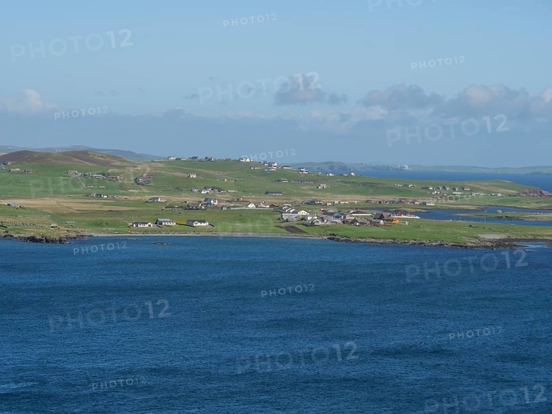 Small settlement with white houses stretches along the grassy coastline in front of the blue sea, green meadows on a deep blue sea and a rocky coastline with individual houses, lerwick, shetland, Scotland, United Kingdom, Europe