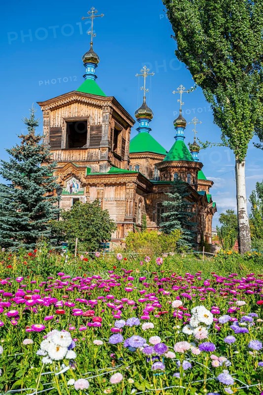 Colourful flowers in front of the Russian Orthodox Church Cathedral of the Holy Trinity, wooden church with green spires, Karakol, Kyrgyzstan, Asia