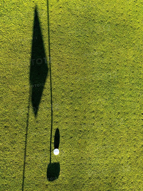 Golf Ball on Putting Green with Shadow and Shadow of a Golf Flag and Golf Club Putter in a Sunny Day in Switzerland