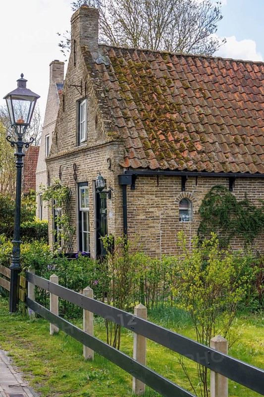 Small brick house with tiled roof and garden, surrounded by fresh spring greenery, rustic atmosphere, historic houses in a small village with small streets and trees in spring, Nes, Ameland, Netherlands