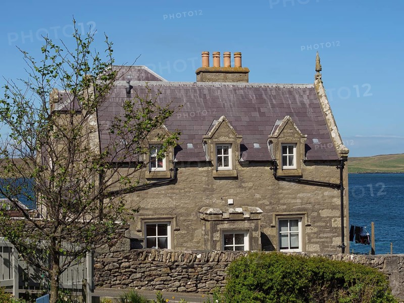 A stone house with fireplaces next to a tree, coastal landscape, blue sky and sea, old stone house by the blue sea against a blue sky, Lerwick, Scotland, United Kingdom, Europe