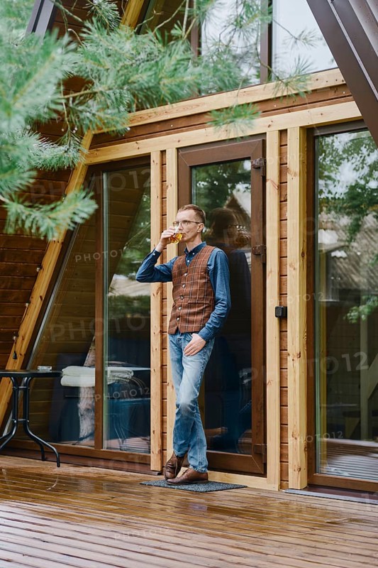 Middle-aged man goes out onto the wet terrace with a glass of whiskey and enjoys the fresh air after the rain