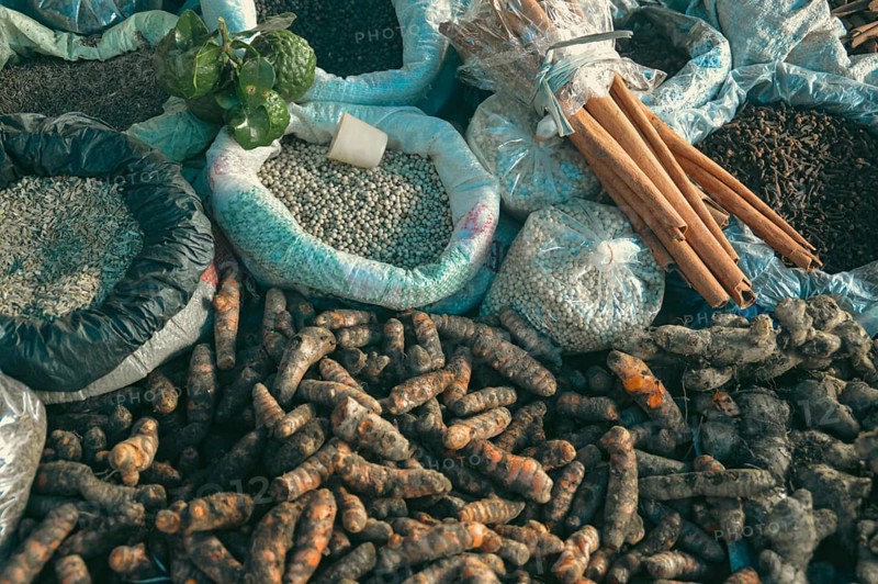 Assorted raw agricultural produce including cinnamon bark, lime, turmeric, clove, peppercorns and other spices use in Ayurveda and alternative holistic healing medicine displayed at a traditional market