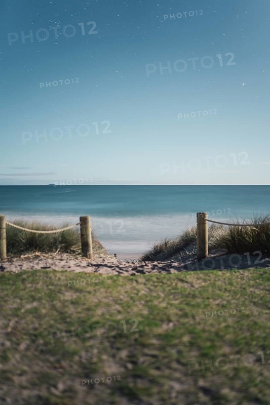 Starry night sky over a quiet beach and sea, demarcated by wooden posts and rope