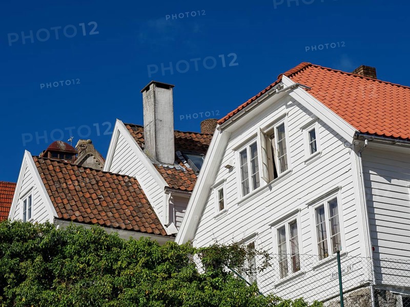 White houses with red tiled roofs, bright blue sky, windows with shutters, historical atmosphere, white wooden houses with red roofs against a blue sky, trees and white fences along the street, stavanger, norway