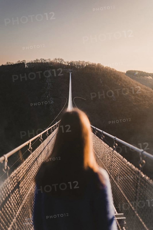 Woman looks into the distance at sunrise on the Geierlay suspension rope bridge in Moersdorf in Rhineland-Palatinate Germany after a hike in autumn