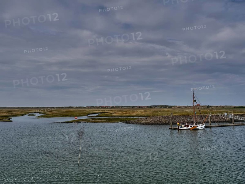 Sailboat at a jetty surrounded by a watery landscape under a cloudy sky, small jetty with a mono-sea sailboat in the north sea against a cloudy sky, spiekeroog, germany