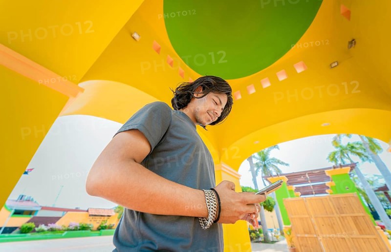 Low angle view of young man using cell phone outdoors. Smiling latin guy texting with cell phone in Nagarote park
