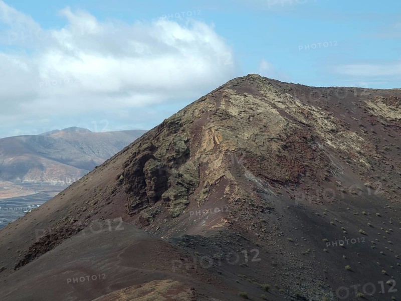 Dry volcanic area with rocky mountain slopes under a partly cloudy sky, barren landscape of lava mountains, lanzarote, spain