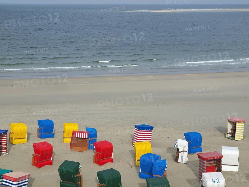 Various colourful beach chairs scattered on empty beach with calm sea in background, beach chairs and beach tents by the sea under cloudy sky, boardwalk in sand, Borkum, germany