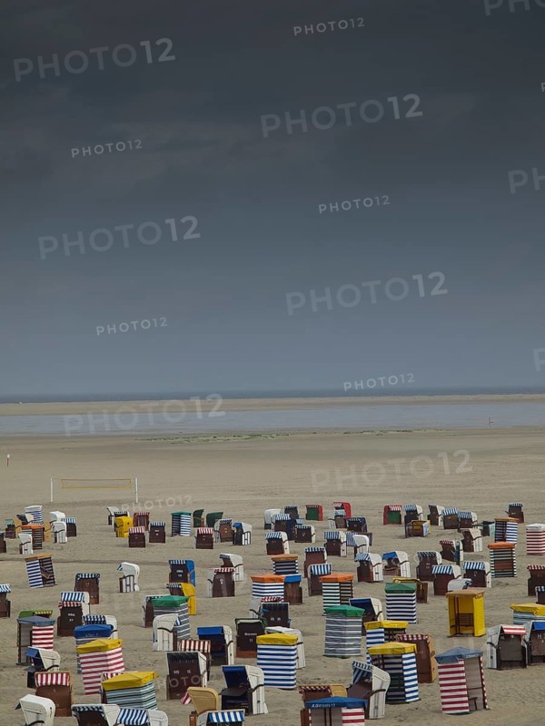Dramatic sky over numerous colourful beach chairs on empty, wide beach with sea view, beach chairs and beach tents by the sea with cloudy sky, boardwalk in the sand, Borkum, germany