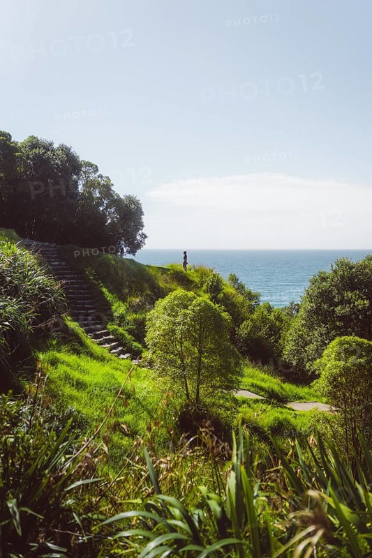 Woman standing at a viewpoint with a paradisiacal view of the beach and the sea. Taken in Tauranga, New Zealand, Oceania