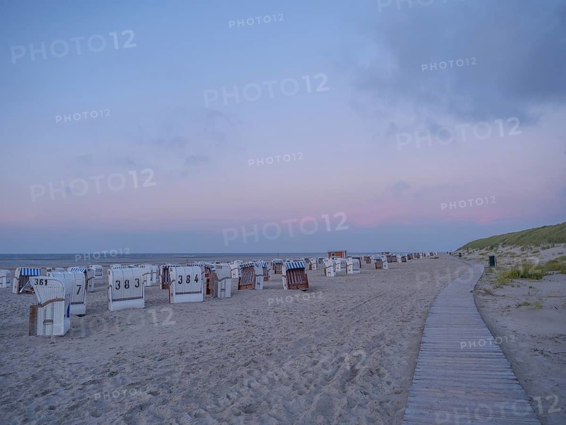 A long beach with white and striped beach chairs in the soft evening light and a wide wooden walkway, setting sun on a beach with beach chairs and clouds in the sky, spiekeroog, germany