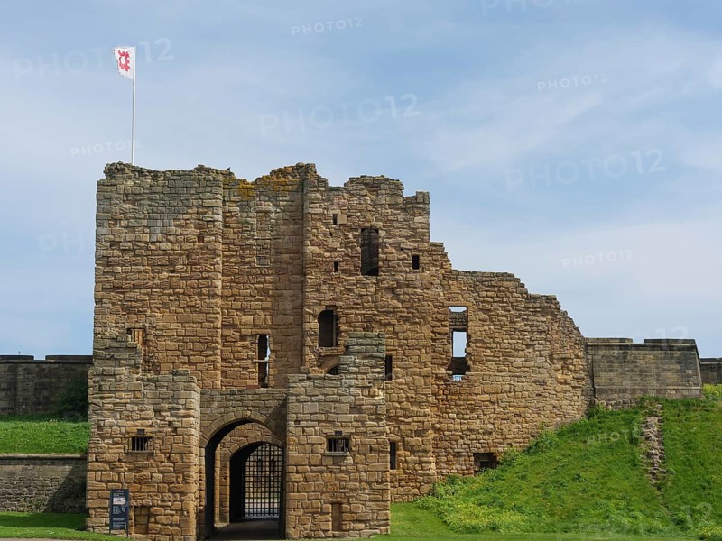 Close-up of a castle ruin with medieval architecture and a flag in the wind under a blue sky, ruins and old stone walls by the sea, green fields with ruins, Newcastle, England, United Kingdom, Europe
