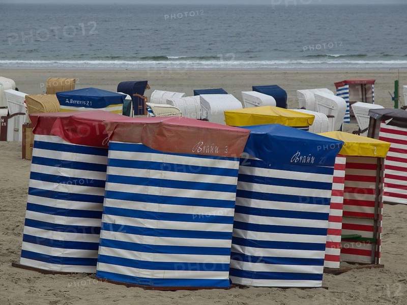 Row of colourful beach chairs with stripe pattern on the beach with a view of the sea, beach chairs and beach tents by the sea under a cloudy sky, boardwalk in the sand, Borkum, germany