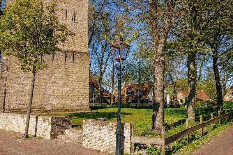 Street lamp next to a brick tower and trees, with a pavement and spring atmosphere, historic houses in a small village with small streets and trees in spring, Nes, Ameland, Netherlands
