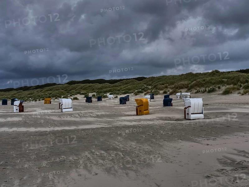 Beach chairs standing on a grey beach under a threatening cloudy sky, dunes in the background, colourful beach chairs on the beach and in the dunes under an overcast sky by the sea, Juist, Germany, Europe
