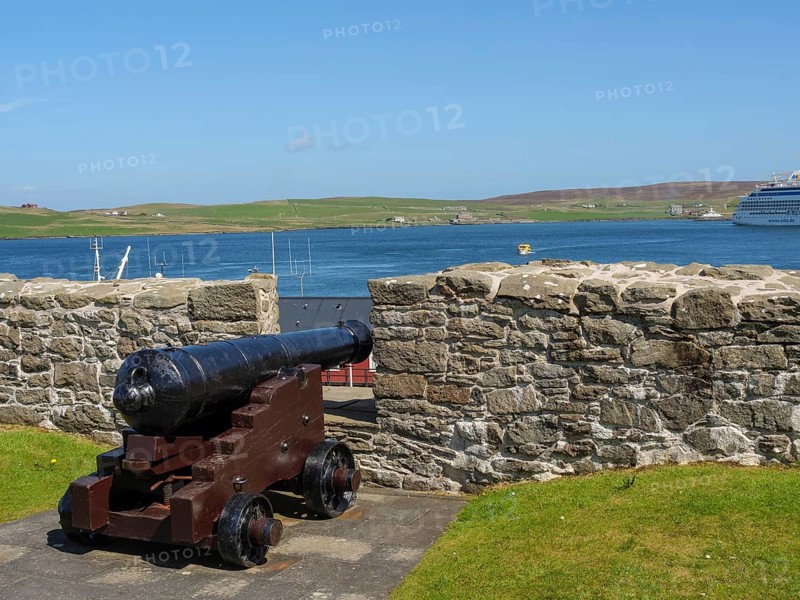 Historic cannon in front of a stone wall with a view of the sea, a ship and green hills, old cannons on a stone wall by the sea against a blue sky, lerwick, Scotland, United Kingdom, Europe