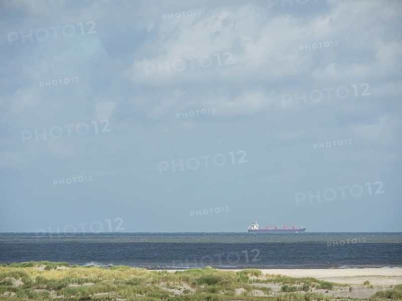 Cargo ship on the sea under cloudy sky near the coast, lonely beach with dune grass in the neighbouring dunes and marker posts, clouds playing in the sky, Spiekeroog, Germany, Europe