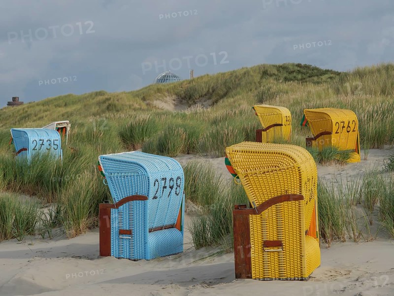 Different coloured beach chairs on the sandy beach, surrounded by dunes and under a cloudy sky, colourful beach chairs on the beach and in the dunes under a cloudy sky, red wooden boat and yellow beach chair, Juist, Germany, Europe