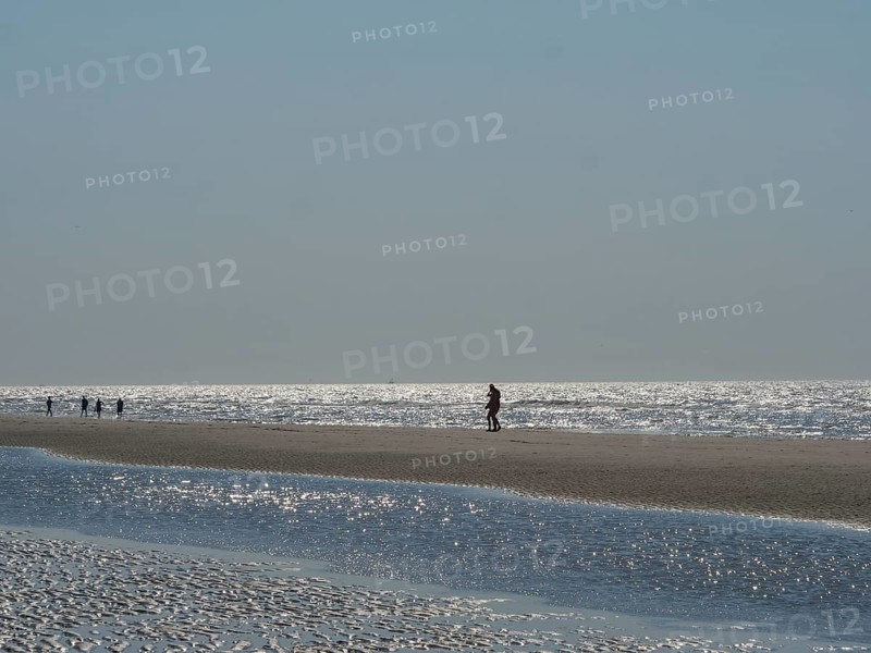 Single person walking along a wide beach, other people visible in the distance, glittering sea water at low tide on the beach, de haan, belgium