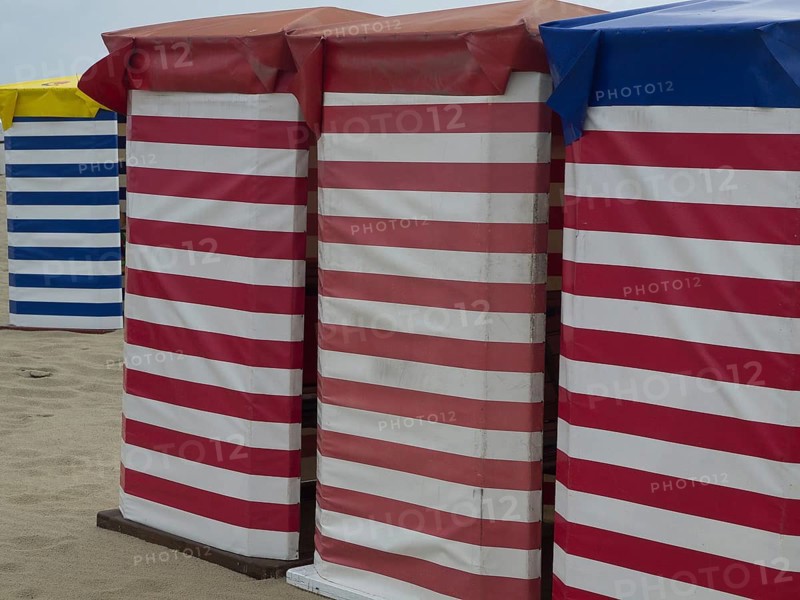 Striped beach huts in red-white and blue-white on the sandy beach, beach chairs and beach tents by the sea under a cloudy sky, boardwalk in the sand, Borkum, germany
