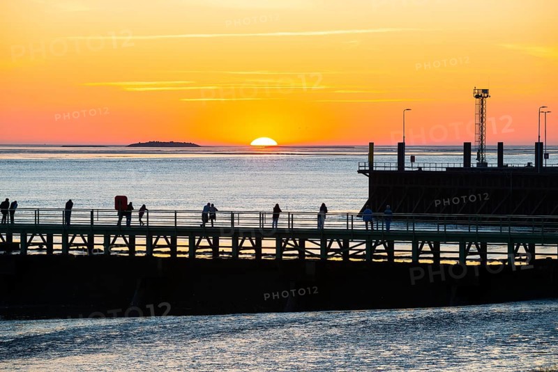 Silhouettes of several people on the pier free canal, jetty, couples and individuals watching the picturesque, golden, breathtakingly beautiful sunset over the sea, Langluetjen II island on the horizon, harbour facilities, sun half sunk, orange glowing cloudless sky, wide sea in soft colours, mouth of the Weser into the North Sea, Outer Weser, Bremerhaven, Land Bremen, Germany, Europe