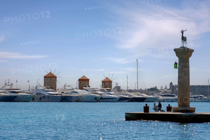 Stag Elafos, sculpture on a column, at the harbour entrance, in the background the three windmills of Rhodes, Mandraki harbour, Rhodes, Rhodes island, Dodecanese, Greece, Europe