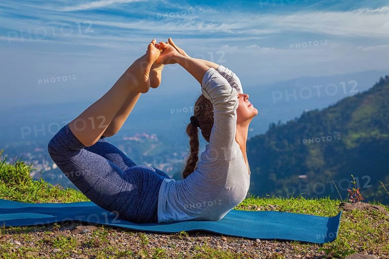 Yoga outdoors, young woman doing Ashtanga Vinyasa Yoga asana Dhanurasana, bow pose, in Himalayas mountains in the morning Himachal Pradesh, India, Asia