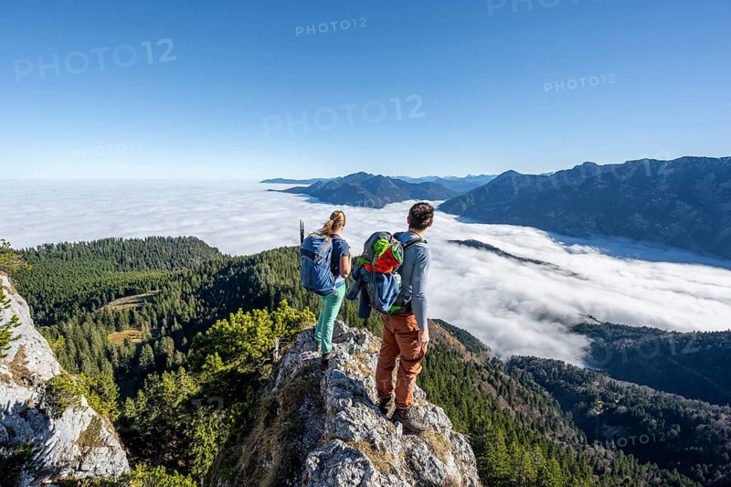 Two hikers at Ettaler Manndl, view over mountain landscape and sea of clouds, high fog in the valley, Ammergau Alps, Bavaria, Germany, Europe