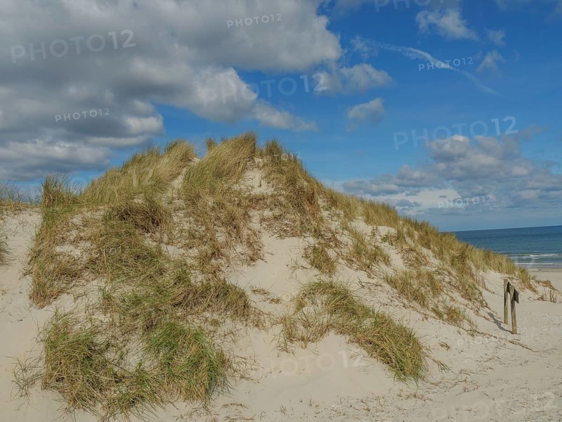 High sand dunes with grass, above a sky with some clouds, dunes on an island with a blue boat and a bench, clouds and sand by the sea, nees, ameland, the netherlands