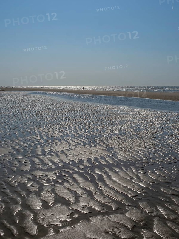 Wide beach with undulating sand surface and reflecting watercourse under a clear sky, glittering sea water at low tide on the beach, de haan, belgium