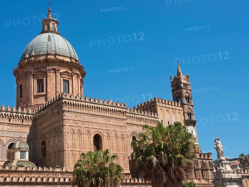 Historic cathedral with large dome and small town character, surrounded by palm trees, under a blue sky, two red towers in front of the panorama of a large city, Barcelona, Spain, Europe