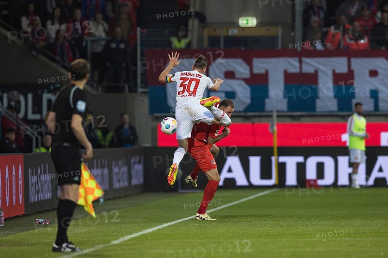 Football match, captain Silvan Dominic WIDMER 1. FSV Mainz 05 left in the air with cramped and uncoordinated posture over the back and head of Jonas FOeHRENBACH 1.FC Heidenheim and for a moment the ball is no longer in focus, left the linesman has the situation in view, football stadium Voith-Arena, Heidenheim