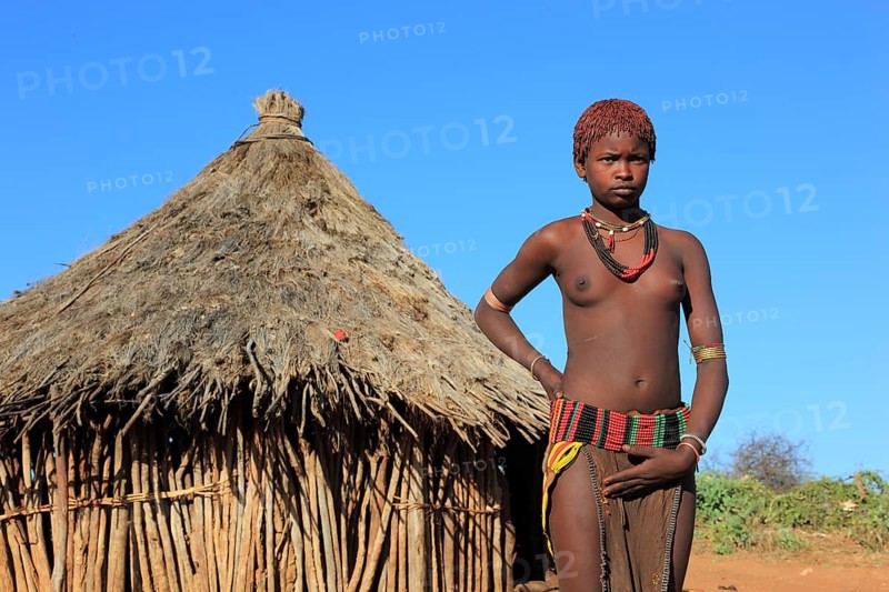 South Ethiopia, Omo region, young woman of the Hammer people standing in front of a round hut, dwelling, Ethiopia, Africa