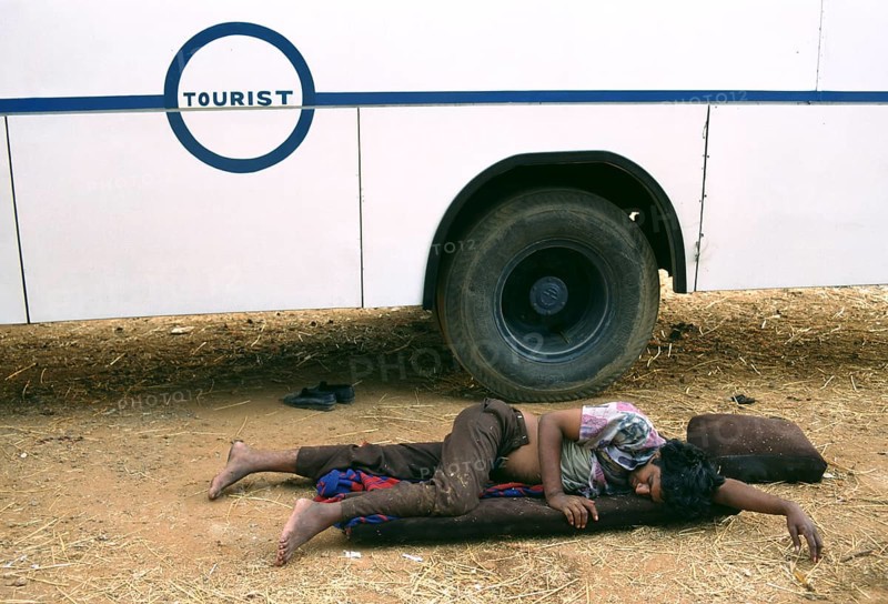 Attendant sleeping near the bus where he is employed, teenage boy working in poor conditions work, Rajasthan, India, Asia