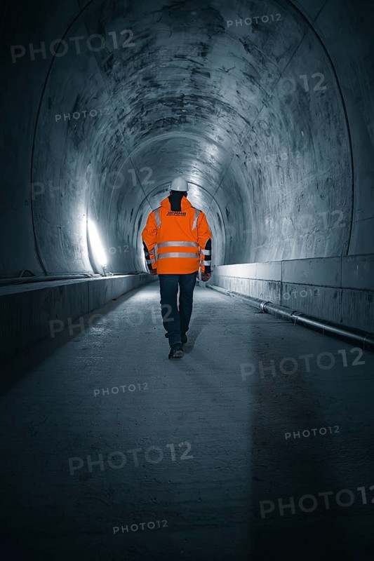 A person in a safety waistcoat walks through an illuminated tunnel with concrete walls, which has a dark atmosphere, Tunnelbau Hermann Hesse Bahn, Ostelsheim, Germany, Europe